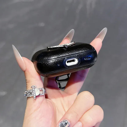 Black crocodile-patterned case held by a hand with decorative nails and rings on a gray background
